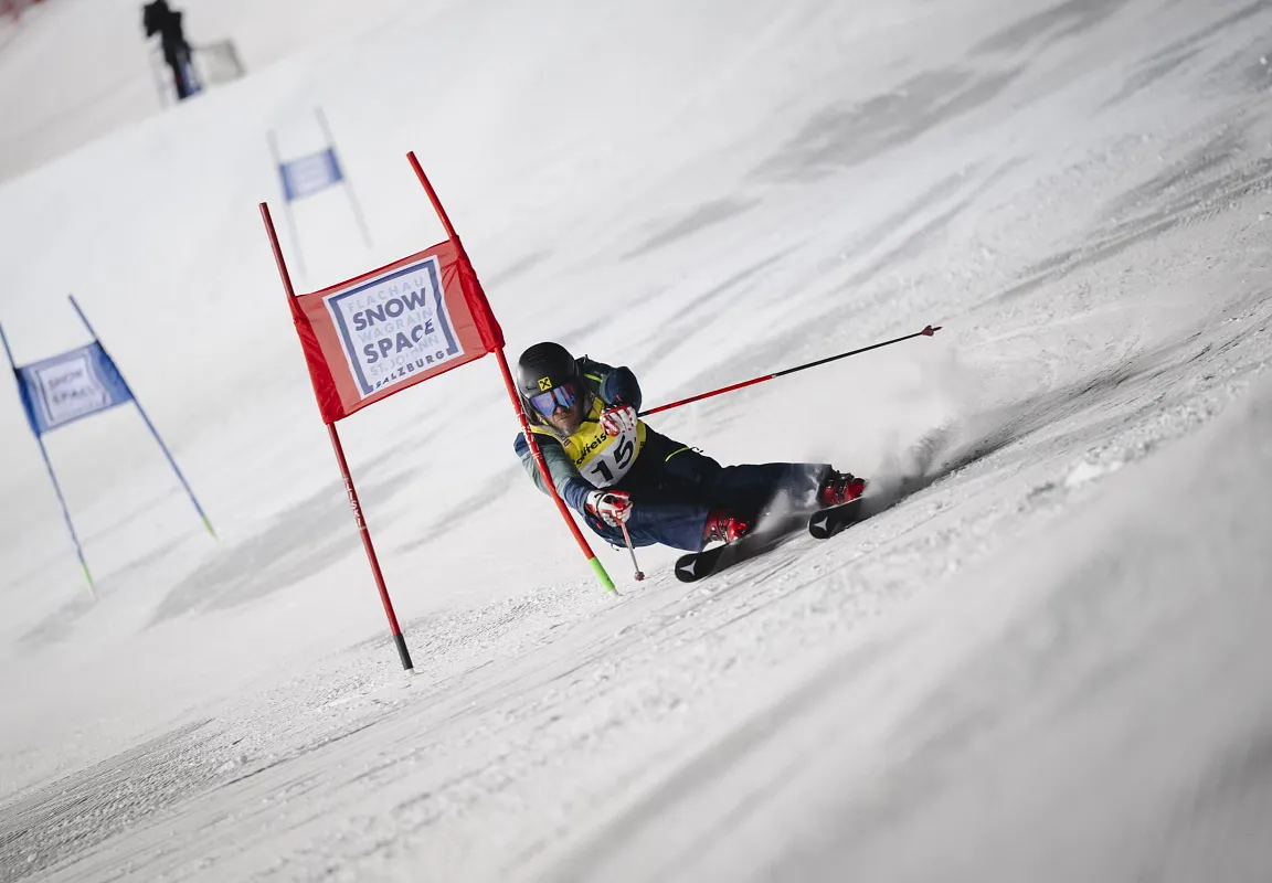 Ein Skifahrer in voller Fahrt durchfährt ein Tor auf einer verschneiten Piste. Er trägt einen Helm und bunte Skikleidung. Die Flaggen zeigen "Snow Space".